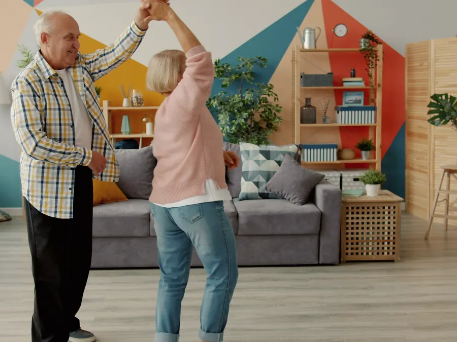 An older couple dance together in their living room.