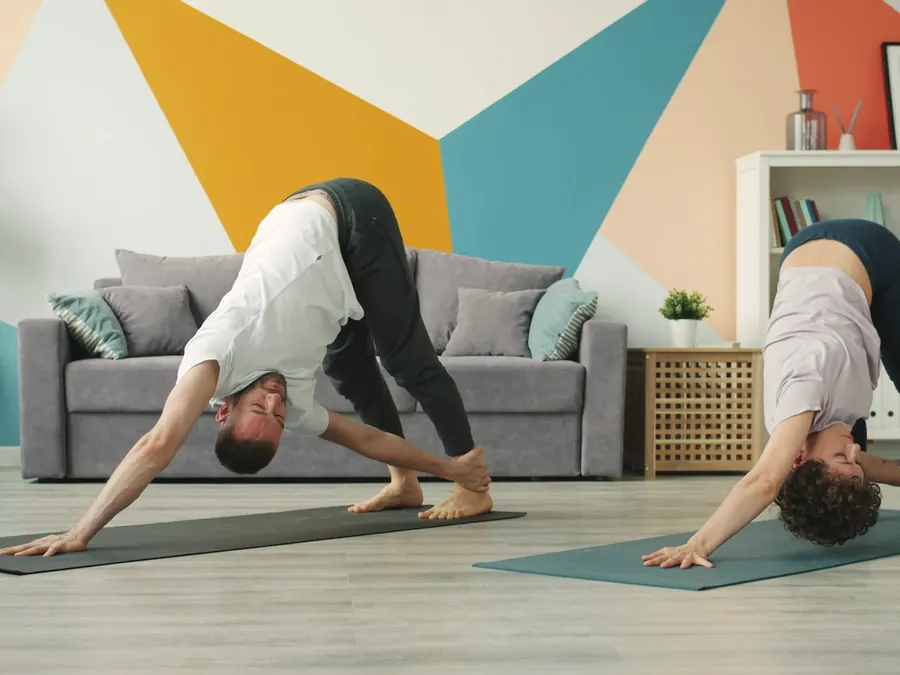 A couple stretch on yoga mats in a colourful living room.