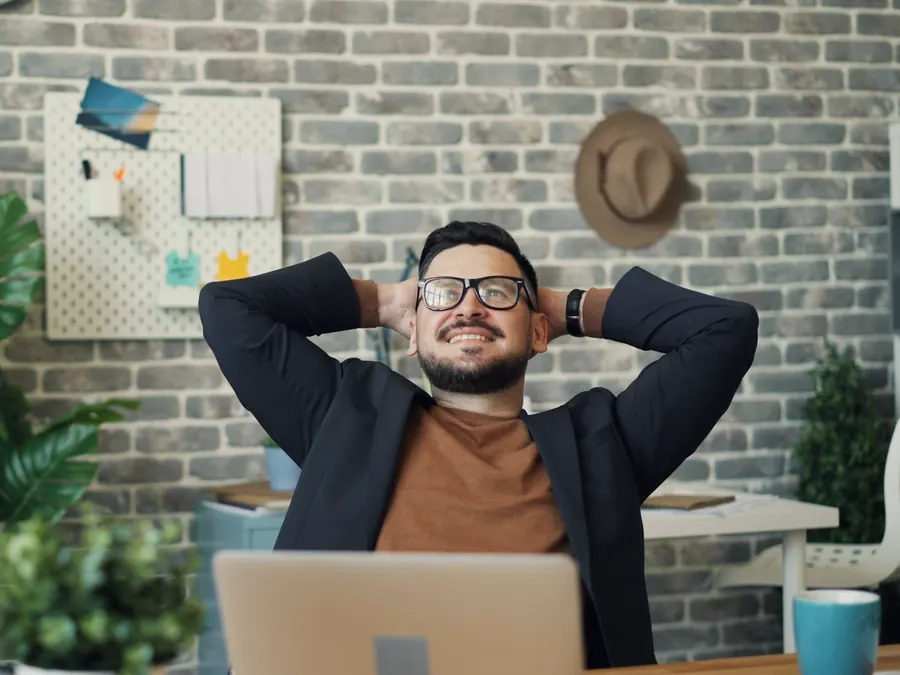 A man leans back in his office chair with his hands behind his head.