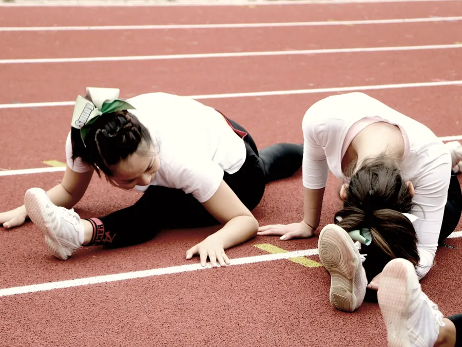 Two athletes stretch side by side on a running track.